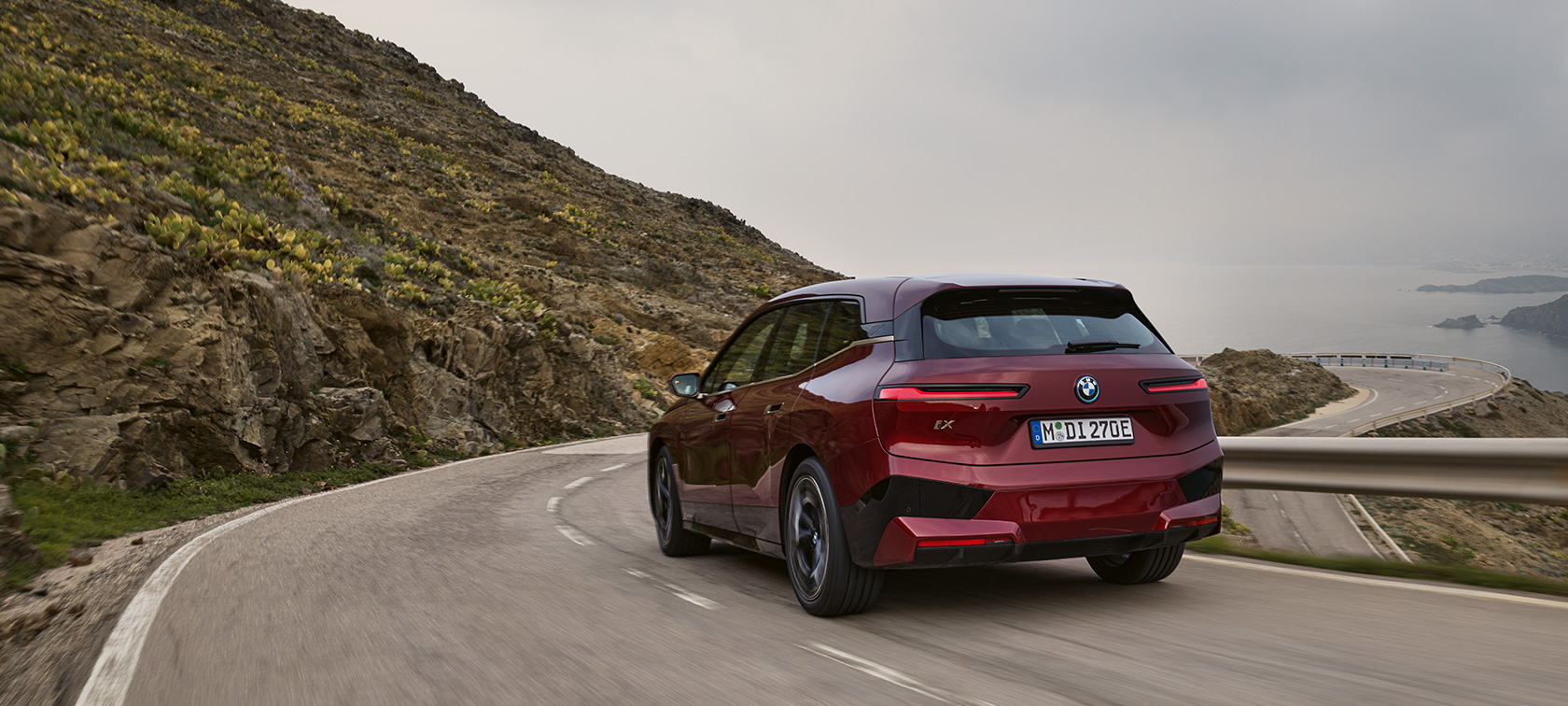 Электрический SUV BMW iX i20 2021 xDrive50 цвета Aventurin Red, вид сзади в движении по набережной